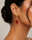 Close-up of an ear wearing a red earring with gold detailing.