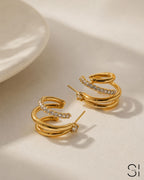 Close-up of Ciara's Diamond Overlay Studs featuring sparkling white rhinestone detailing. Gold hoop earrings with embedded stones on a beige surface