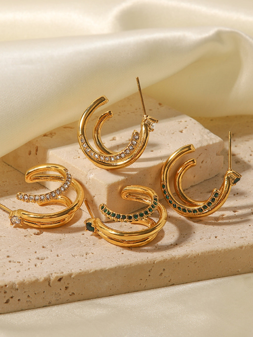 Gold hoop earrings with gemstones on a beige stone surface