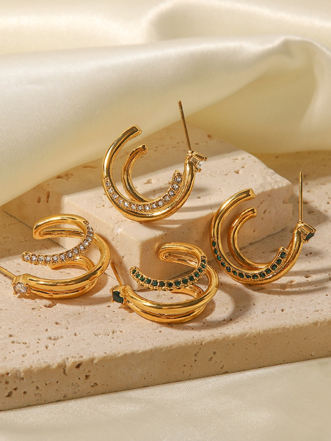 Gold hoop earrings with gemstones on a beige stone surface