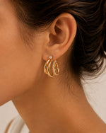 Ciara's Diamond Overlay Studs with white rhinestone detailing and 18K gold plated anti-tarnish finishClose-up of an ear wearing gold hoop earrings with small diamonds.