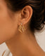 Ciara's Diamond Overlay Studs with white rhinestone detailing and 18K gold plated anti-tarnish finishClose-up of an ear wearing gold hoop earrings with small diamonds.