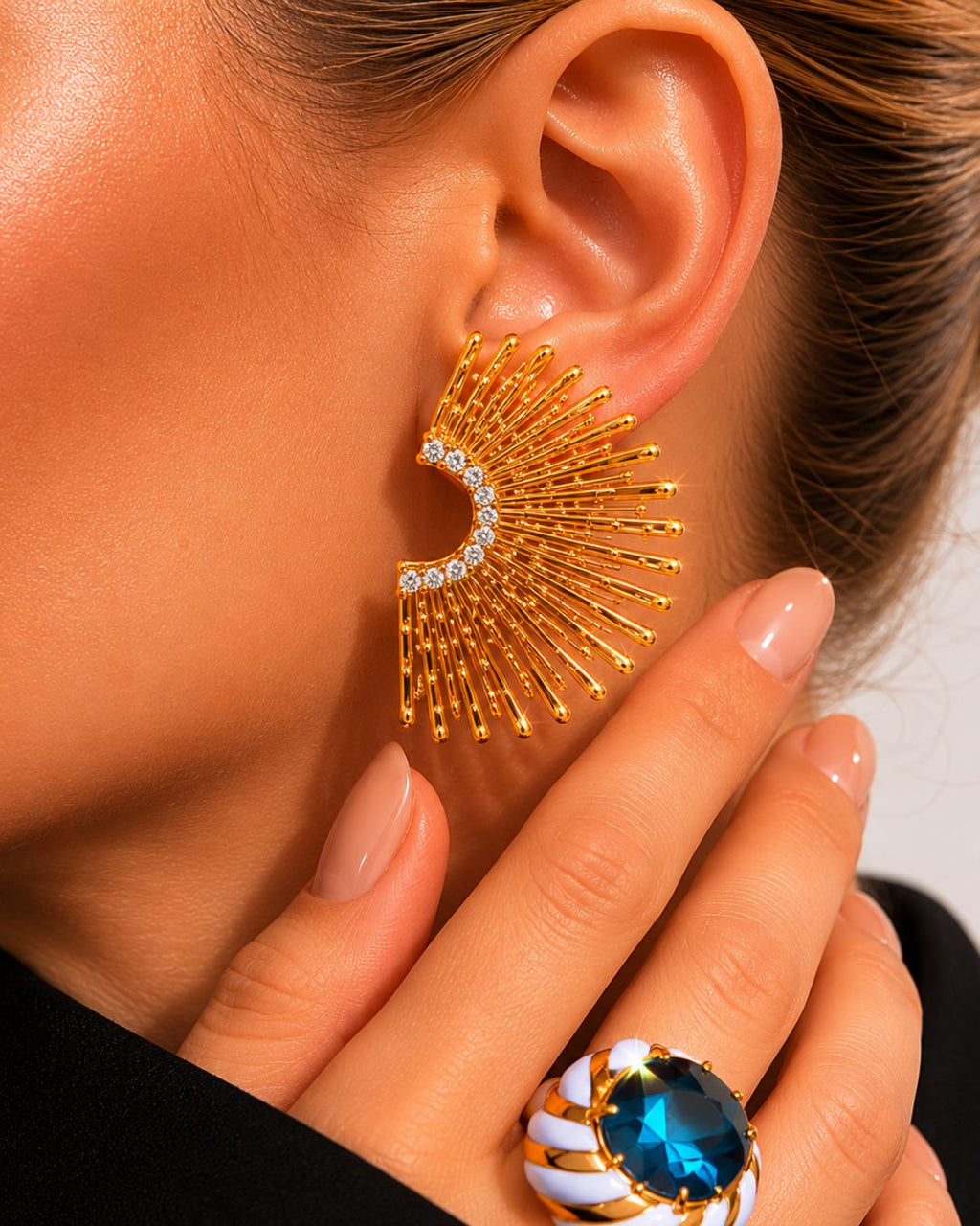 Gold statement earrings with gemstones worn by a person, close-up view.