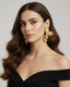 Woman wearing gold Hammered Floral Statement Earrings with textured floral detailing and gold plated finish with a plain background