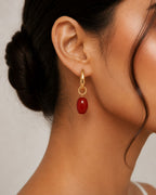 Close-up of an ear wearing a red earring with gold detailing.