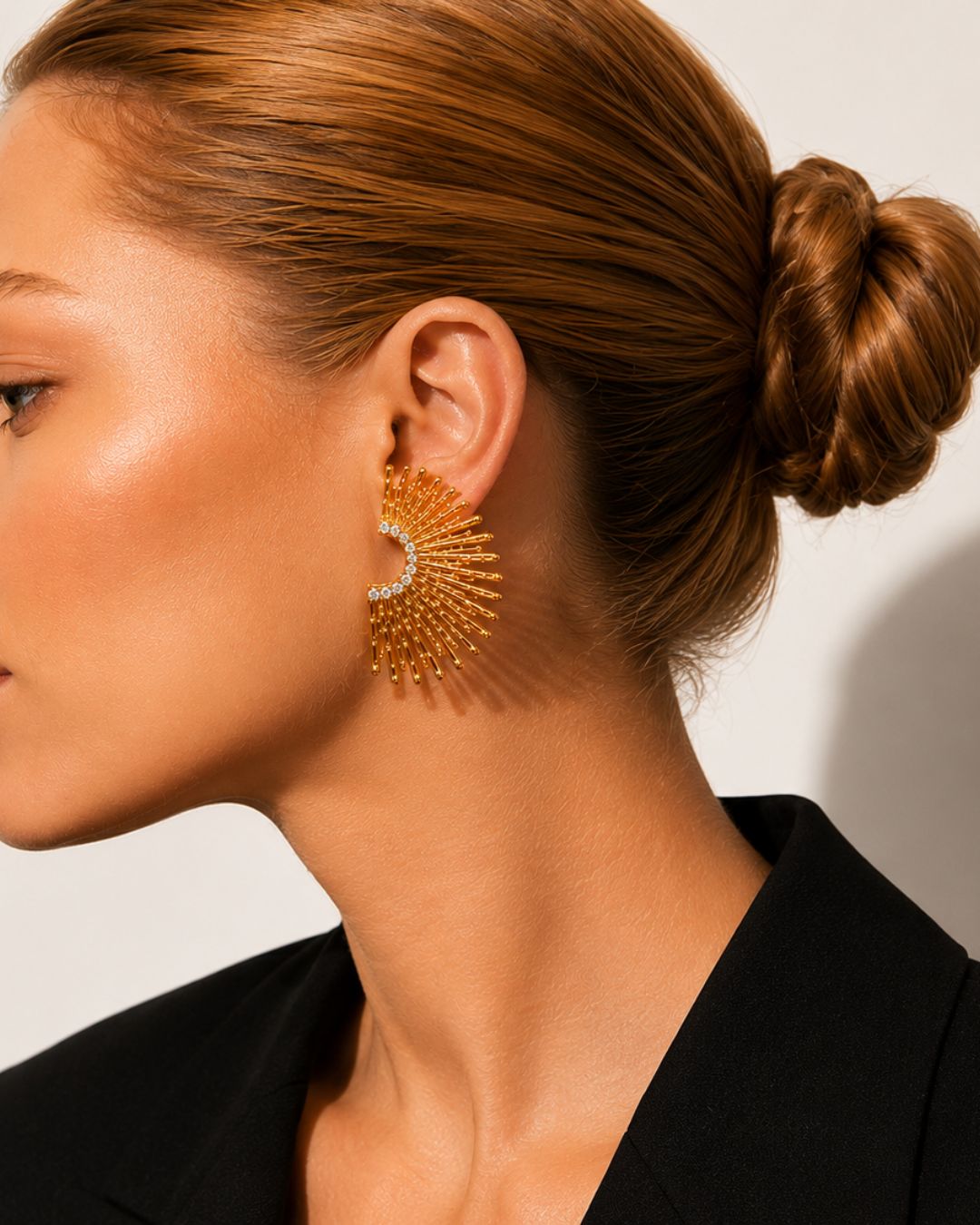 Close-up of a person wearing gold statement earrings with a neutral background