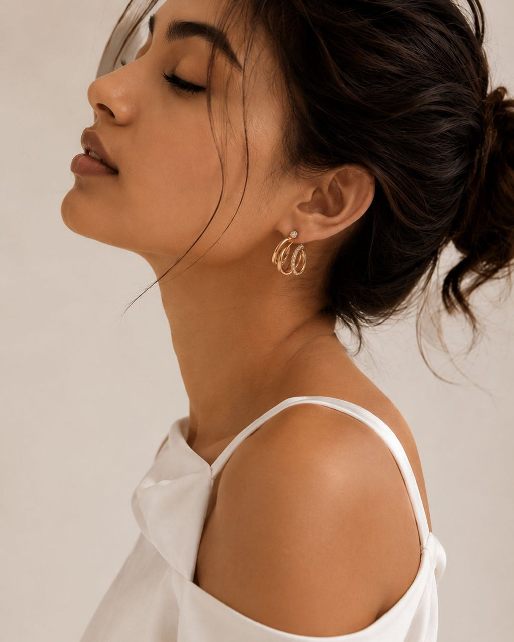 Close-up of a woman wearing gold hoop earrings with a neutral background
