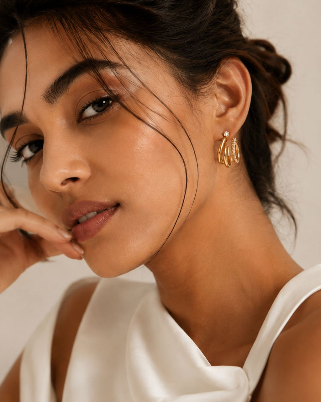Ciara's Diamond Overlay statement stud earrings with elegant diamond inspired design. Close-up of a woman wearing gold hoop earrings with a neutral background