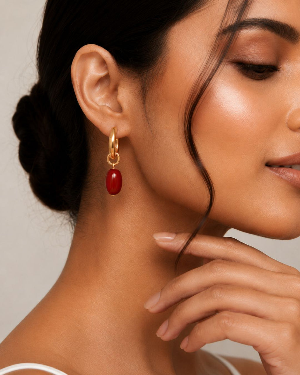 Close-up of a woman wearing a gold earring with a red gemstone against a neutral background